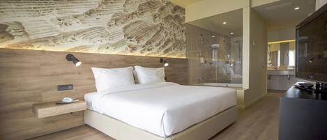 Una habitación de hotel moderna con una cama grande, un cabecero de madera, una mesita de noche con un teléfono y una zona de ducha con paredes de cristal.