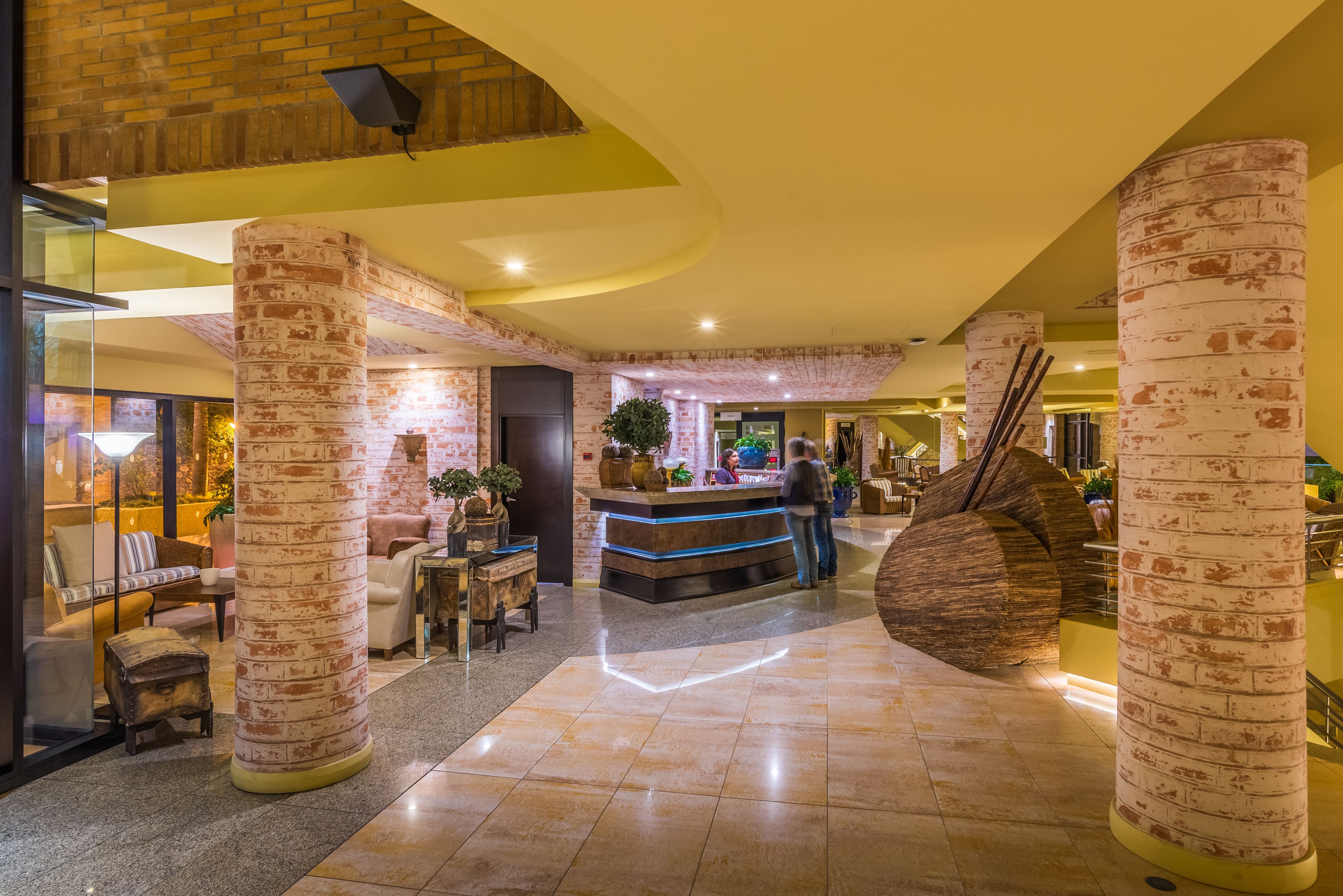 A lobby with brick pillars, a reception desk, and a large wooden sculpture.