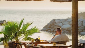 A man sitting at a wooden table with a view of the sea.