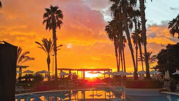 A pool area with palm trees and a sunset view.
