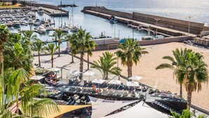 A marina with boats, a beach area with umbrellas and seating, and a view of the ocean. - Calheta Beach - All Inclusive (Calheta)