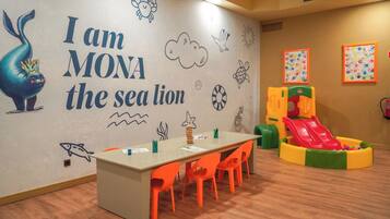 A children's play area with a slide, a table with chairs, and a wall with a sea lion mural.