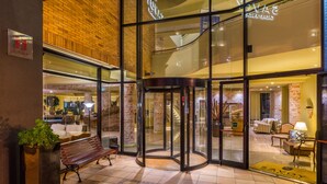 A hotel lobby with a glass revolving door, a bench, and a reception area with a staircase. - Calheta Beach - All Inclusive (Calheta)