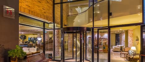 A hotel lobby with a glass revolving door, a bench, and a reception area with a staircase.