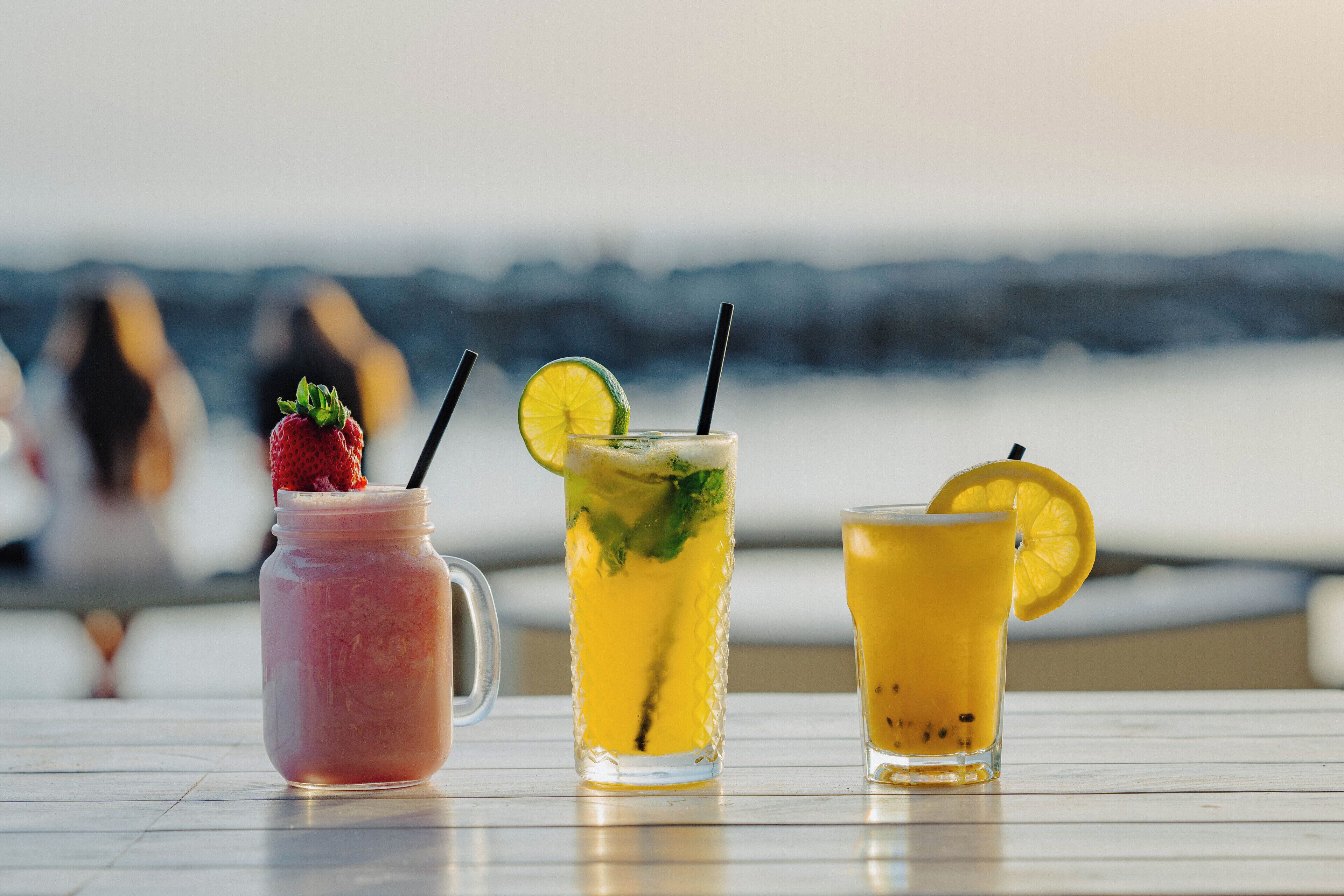 Trois boissons sur une table, avec une vue sur la plage en arrière-plan.