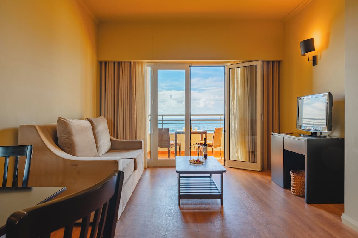 Habitació d'hotel amb un sofà, una taula de cafè, televisió i un balcó amb vista al mar.