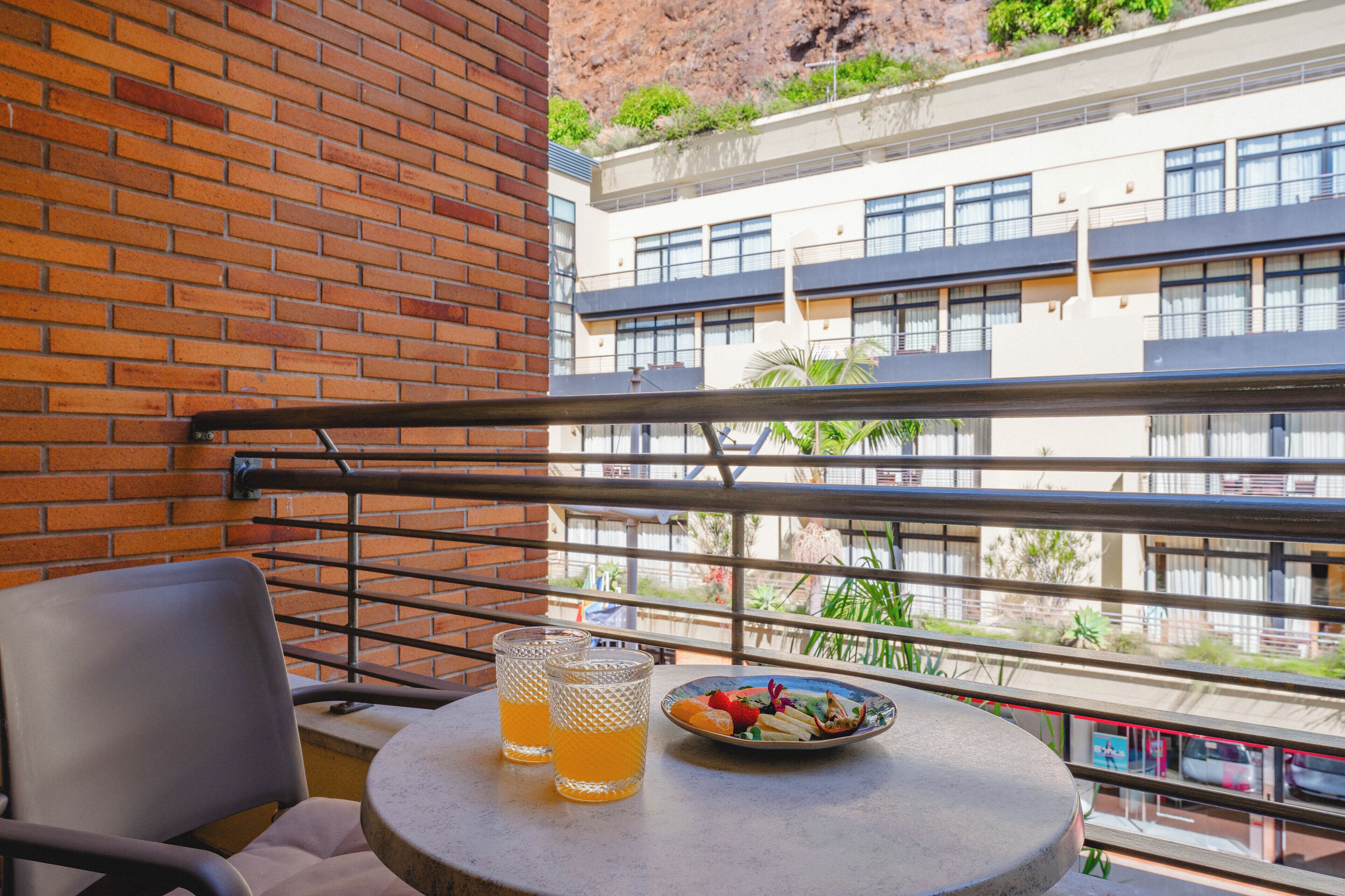 A balcony with a table, two glasses of orange juice, and a plate of fruit.
