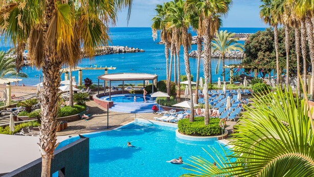 A resort pool area with multiple pools, lounge chairs, and palm trees. - Calheta Beach - All Inclusive (Calheta)