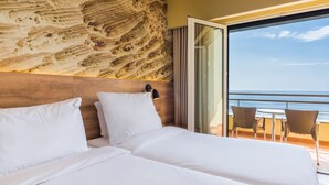 A hotel room with a large bed, a view of the ocean through a balcony, and a textured wall.
