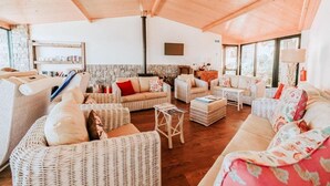 A cozy living room with wicker furniture, a stone fireplace, and large windows. - Hotel Alpino Atlantico Ayurveda Cure Centre - Adults Only (Santa Cruz)