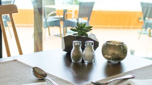 A dining table set with cutlery, a napkin, and salt and pepper shakers, with a view of outdoor seating. - Hotel Alpino Atlantico Ayurveda Cure Centre - Adults Only (Santa Cruz)