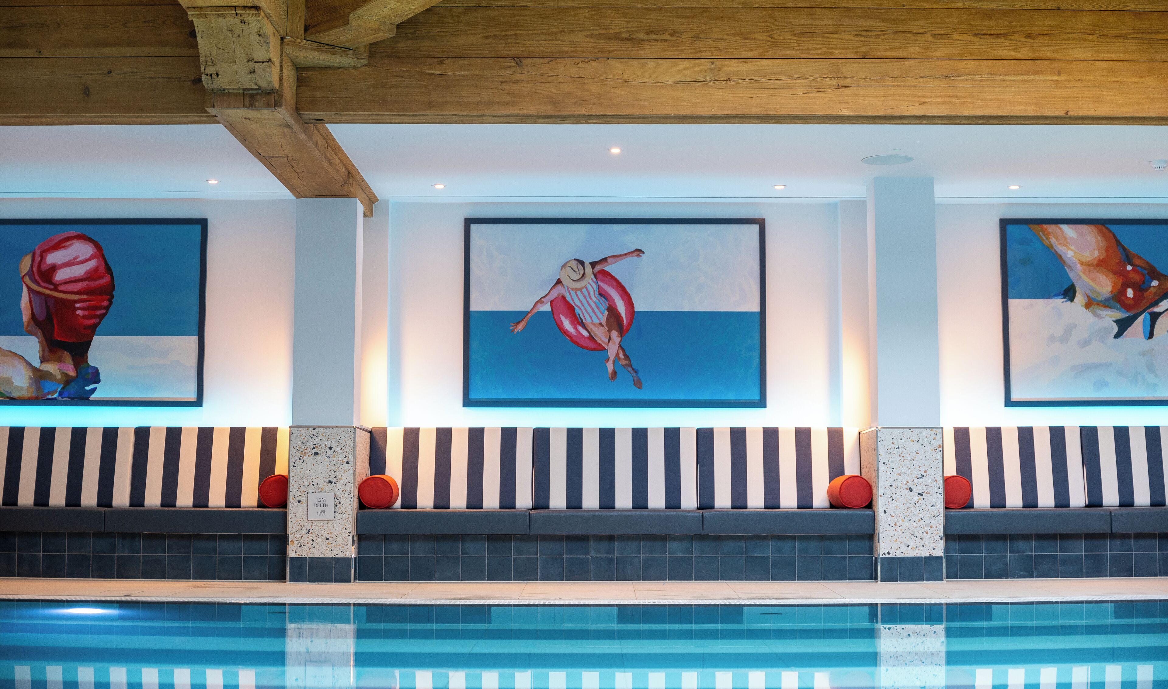 A swimming pool area with artwork on the walls, a striped bench, and a ceiling with wooden beams.