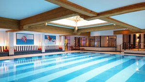 A large indoor swimming pool with a wooden ceiling and a skylight. There are seating areas with cushions and artwork on the walls. - Solent Hotel and Spa (Fareham)