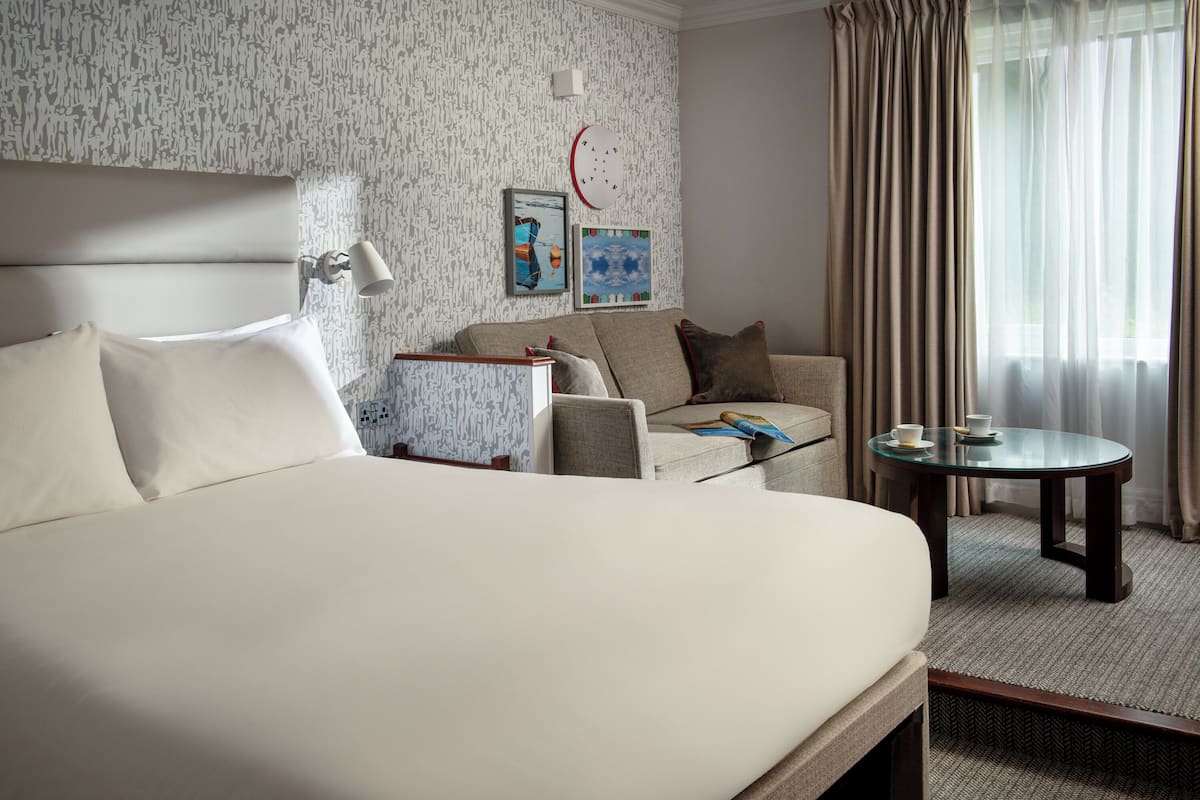 A hotel room with a large bed, a sofa, a small table, and a clock on the wall.