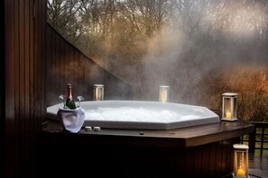 Un jacuzzi con una botella de champán y velas, rodeado de niebla y árboles.