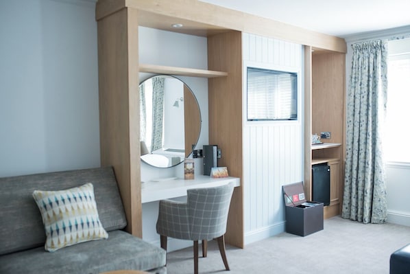 Un dormitorio moderno con escritorio empotrado, un espejo redondo, un sofá gris y un mueble pequeño.