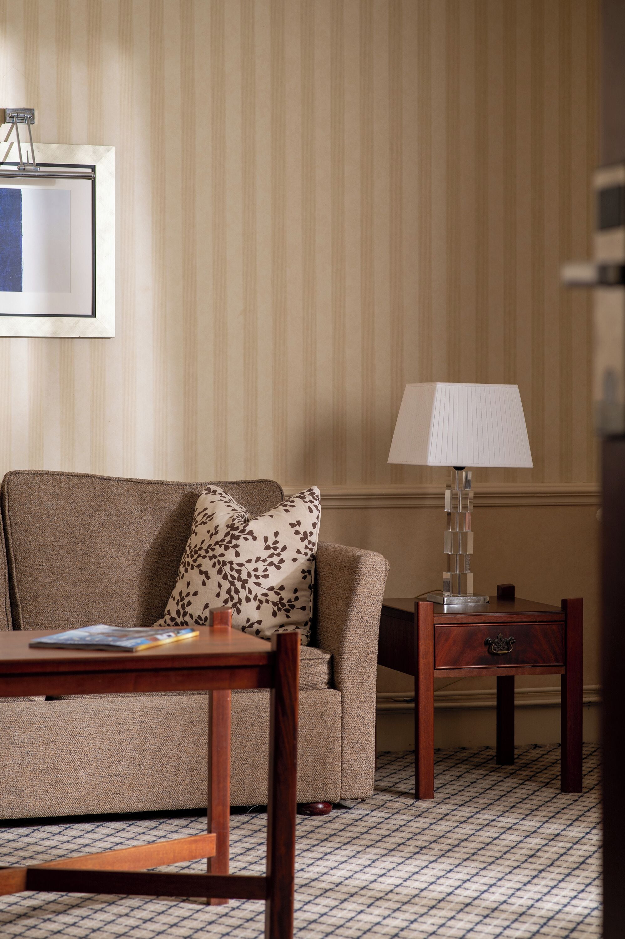 A hotel room with a sofa, a small table, a lamp, and a patterned floor.