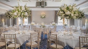 A banquet hall with round tables, white tablecloths, and tall floral arrangements. - Solent Hotel and Spa (Fareham)