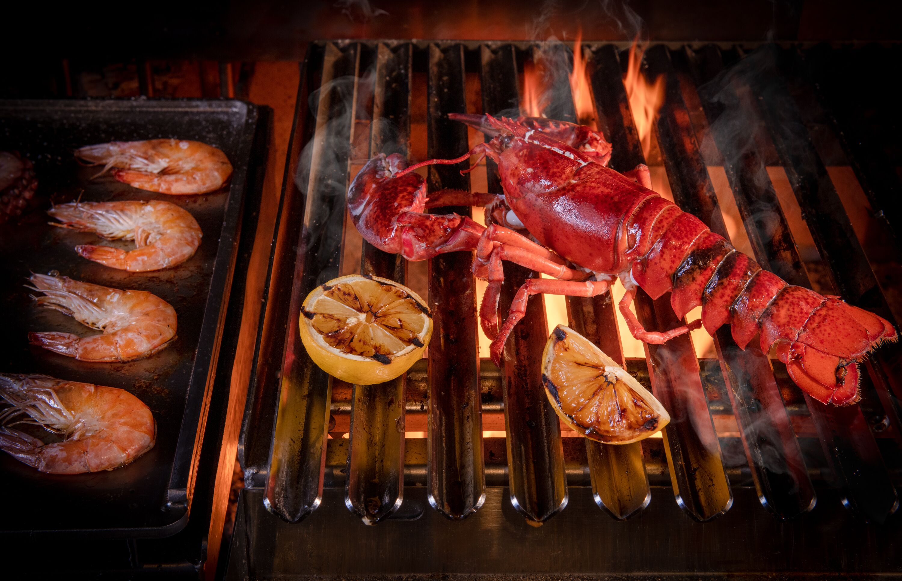 Grilled seafood including shrimp and lobster on a grill with a slice of lemon.