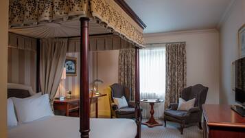 A four-poster bed with a canopy, two armchairs, a small table, and a television in a hotel room.