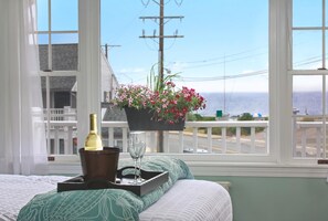 A bedroom with a bed, a window with a view of the ocean, a flower pot, a bottle of wine, and a glass on a tray. - Ocean Inn on Nantasket Beach (Hull)