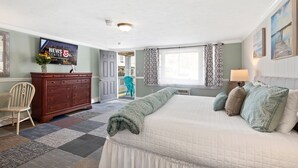 A bedroom with a large bed, a dresser, a TV, and a view of the outside balcony. - Ocean Inn on Nantasket Beach (Hull)