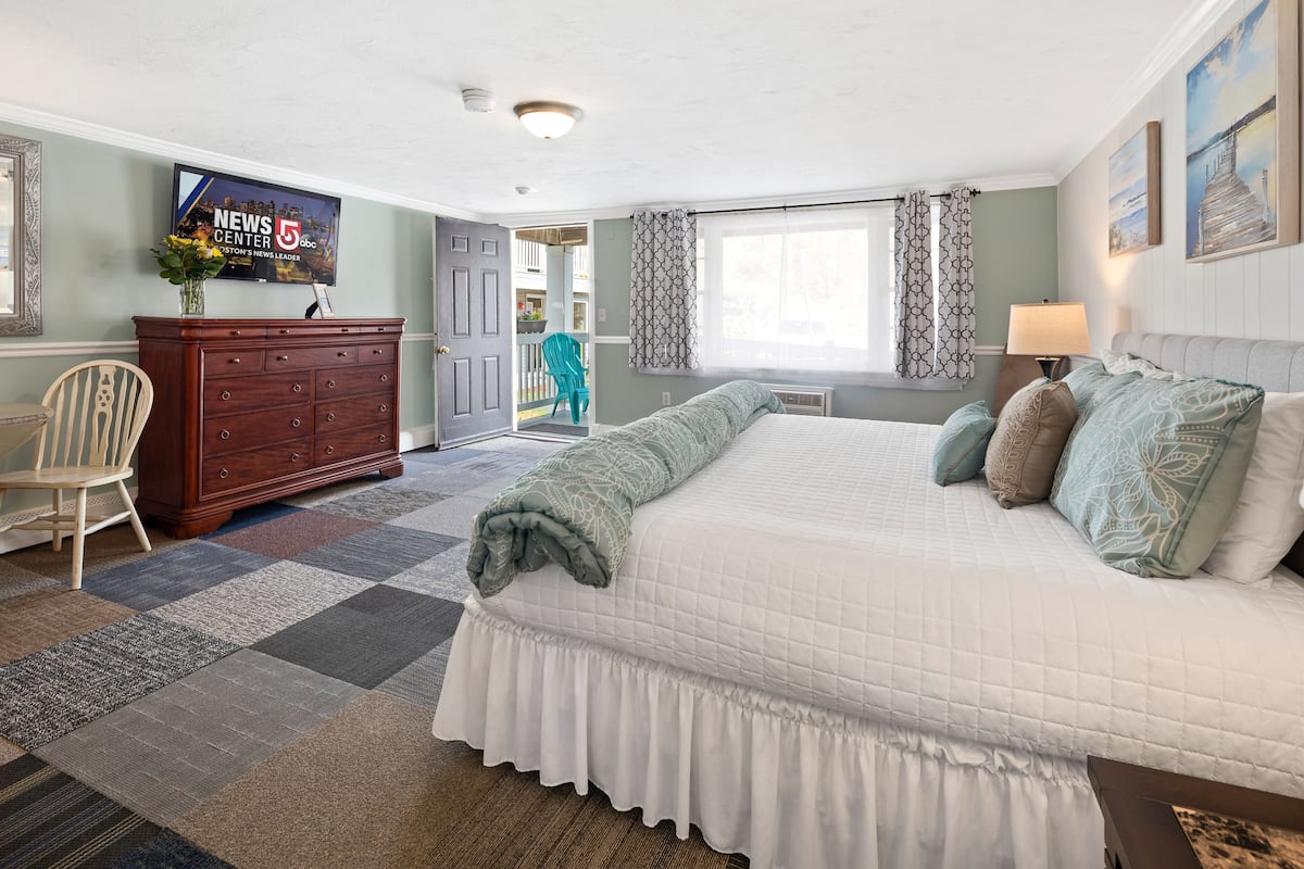 A bedroom with a large bed, a dresser, a TV, and a view of the outside balcony.