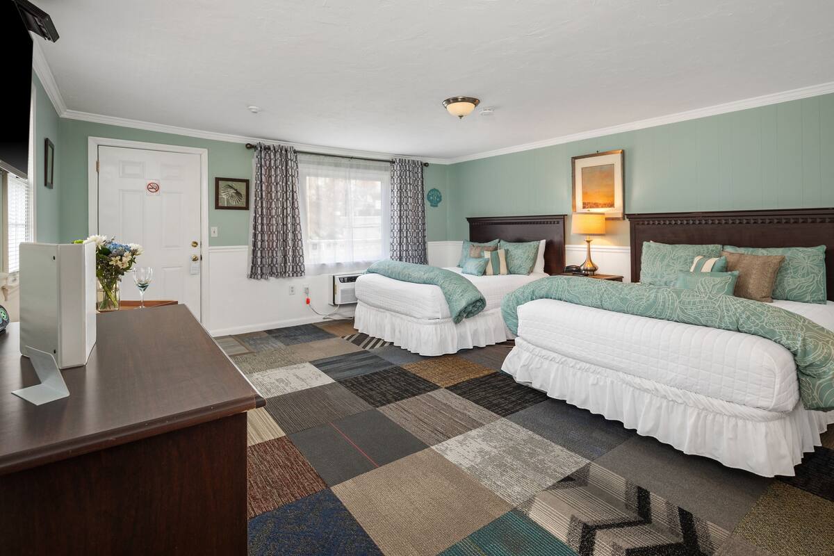 A hotel room with two beds, a desk, a window with curtains, and a view of the outdoors.