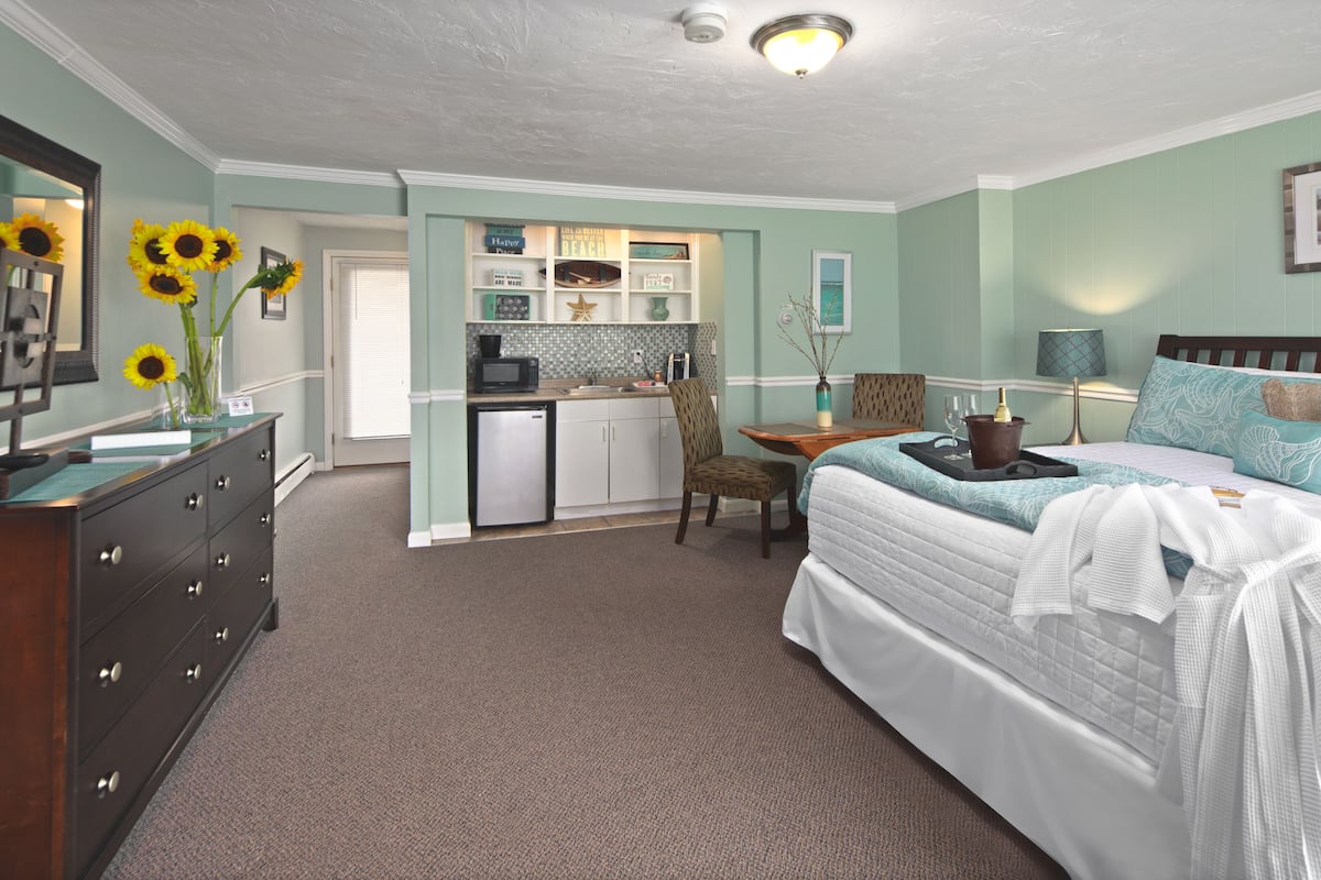 A bedroom with a bed, dresser, and a kitchenette area.