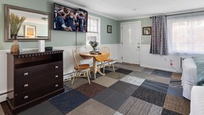 A room with a dining table, chairs, a dresser, a mirror, a television, and a bed. - Ocean Inn on Nantasket Beach (Hull)