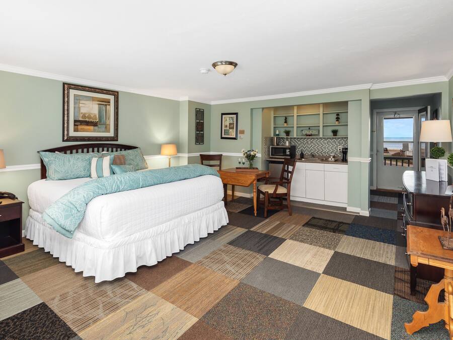 A hotel room with a bed, desk, and kitchenette.