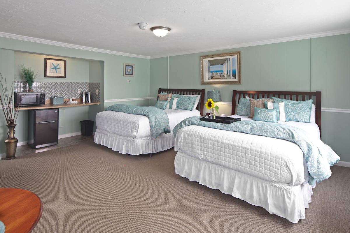 A hotel room with two beds, a kitchenette, and a view of the sea.