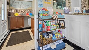 A hotel reception area with a self-service kiosk stocked with snacks and beverages, a sign reading "I'm Longing to be Where the Sea Meets the Sand," and a tiled floor. - Ocean Inn on Nantasket Beach (Hull)