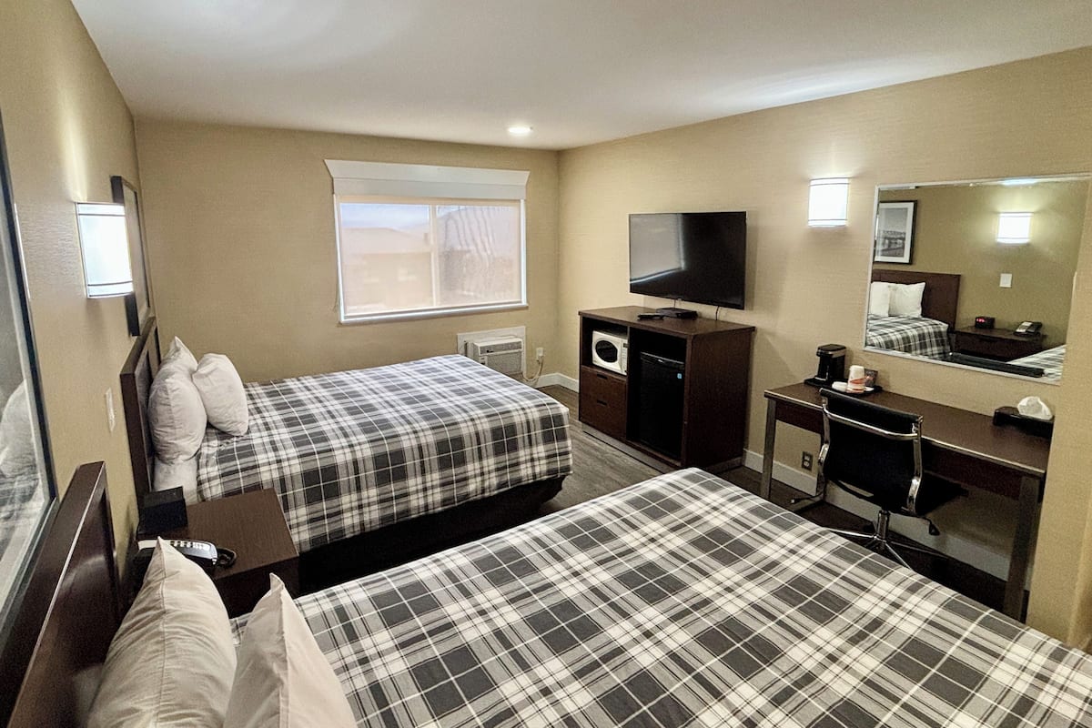 A hotel room with two beds, a TV, a desk, a mirror, and a window.