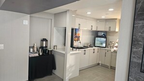 Une cuisine moderne avec des meubles blancs, un four à micro-ondes, un réfrigérateur et une machine à café.