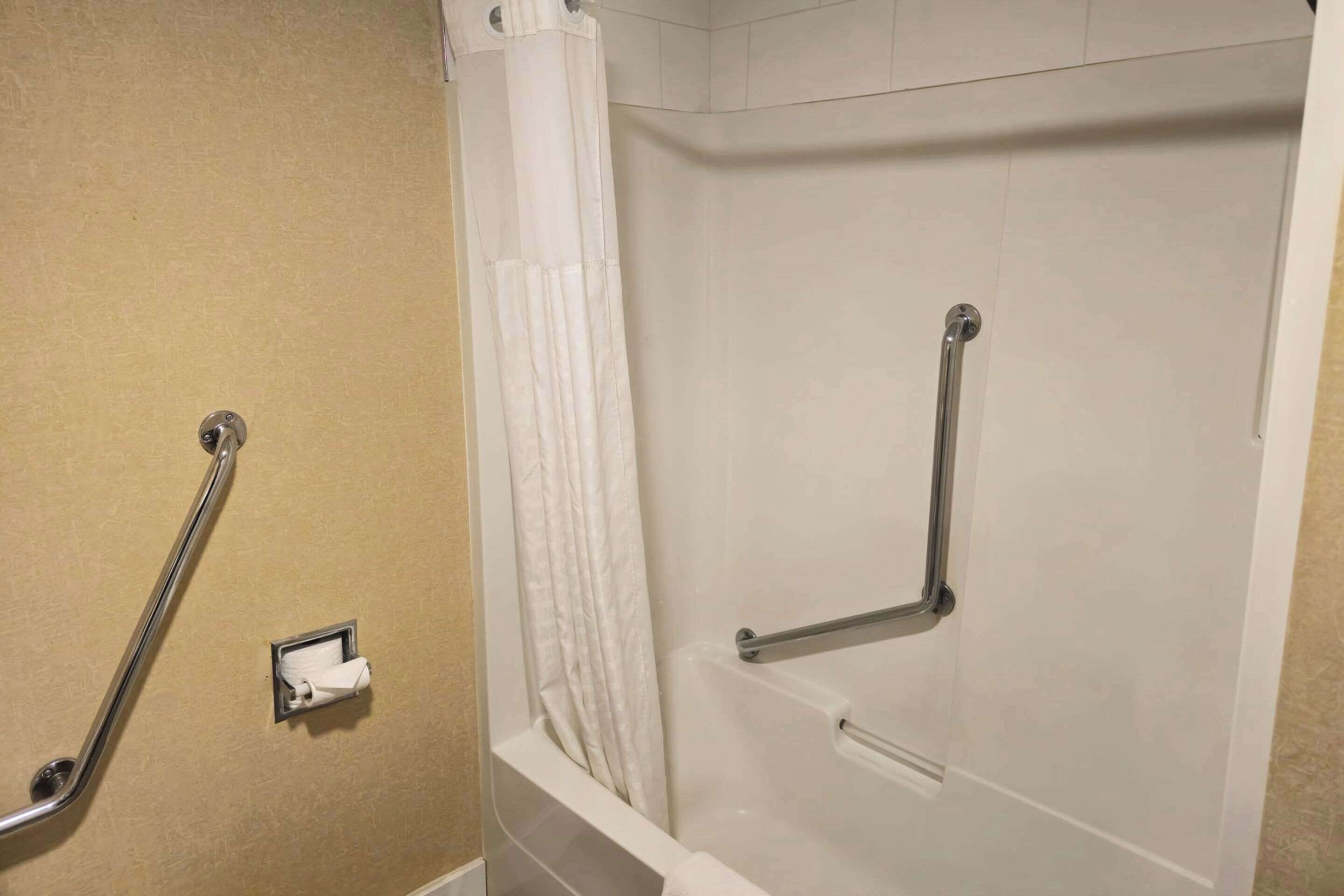 A bathroom with a beige wall, a white shower curtain, and a grab bar.