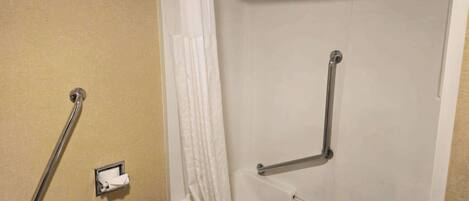 A bathroom with a beige wall, a white shower curtain, and a grab bar.