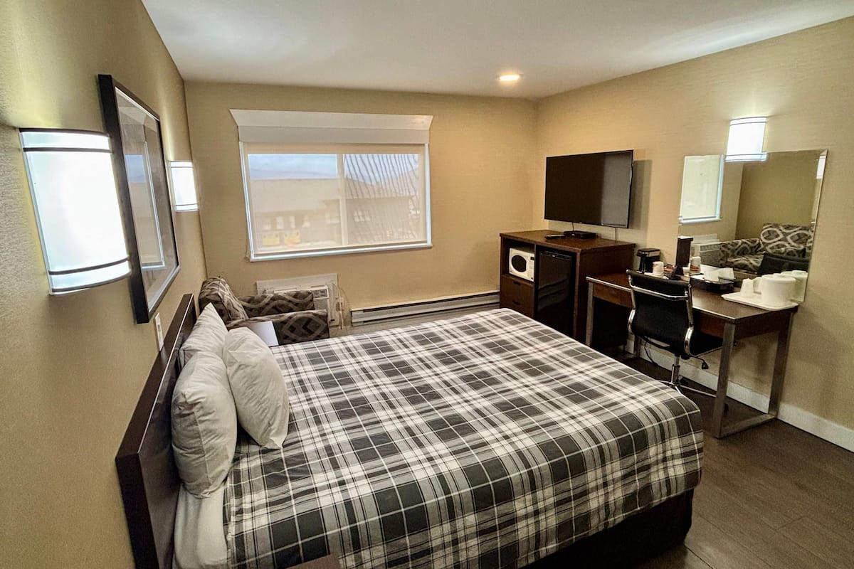 A hotel room with a bed, a desk, a television, a microwave, and a window with blinds.