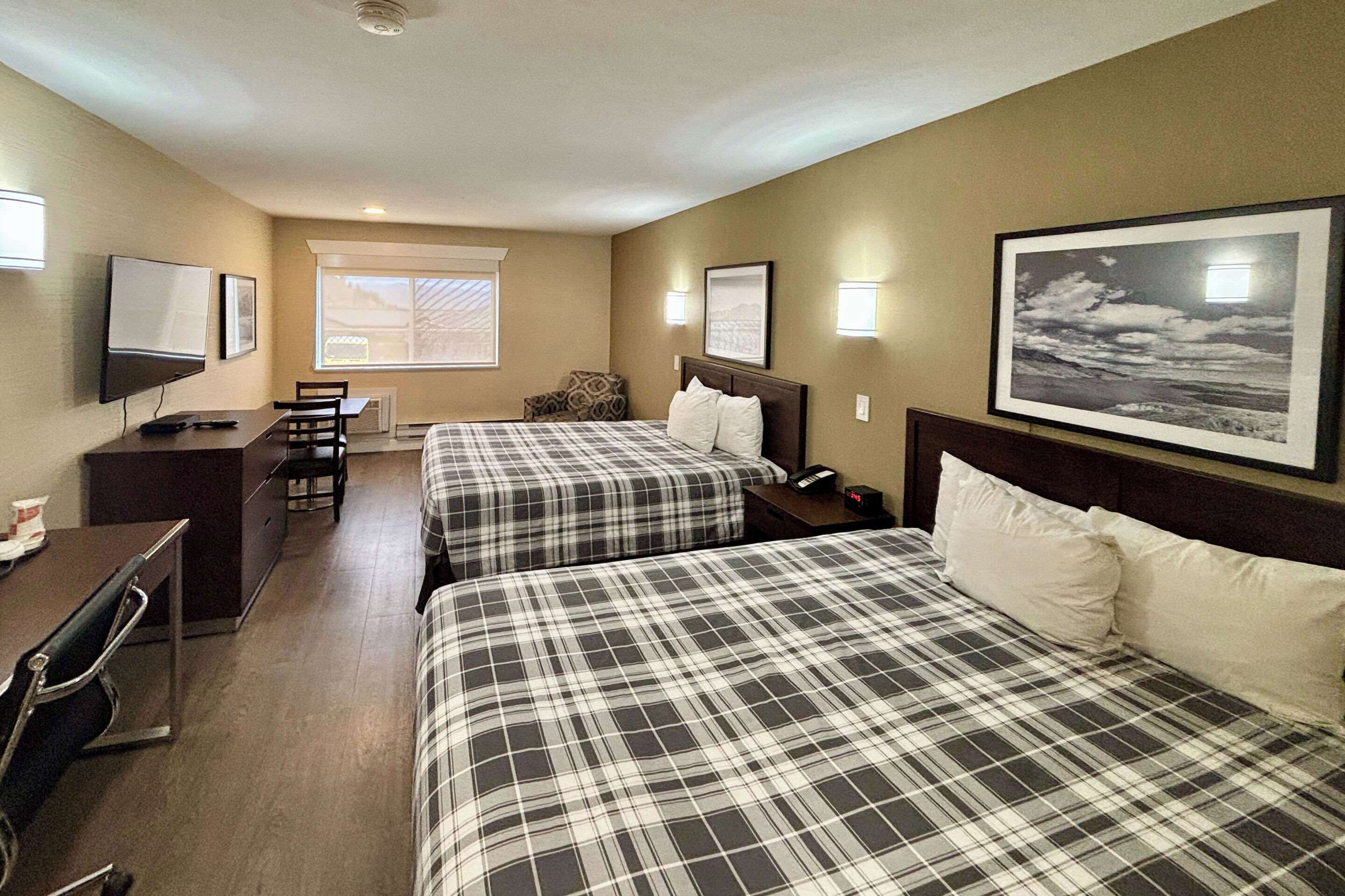 Habitación de hotel con dos camas, un escritorio, una silla, un televisor y una ventana.
