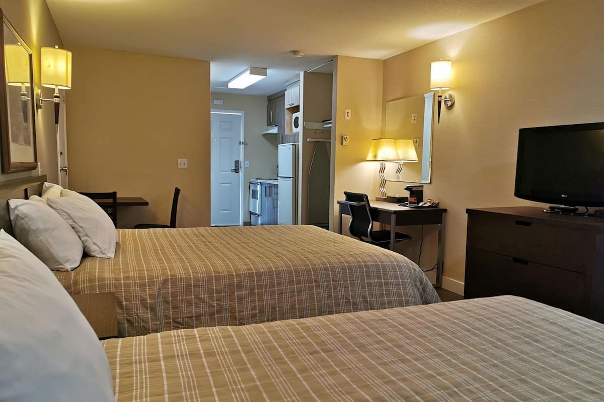 A hotel room with two beds, a desk, a chair, a television, and a kitchenette.