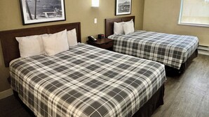Une chambre d’hôtel avec deux lits, chacun recouvert d’une couverture à carreaux, une table de chevet avec un téléphone et deux tableaux encadrés au mur.