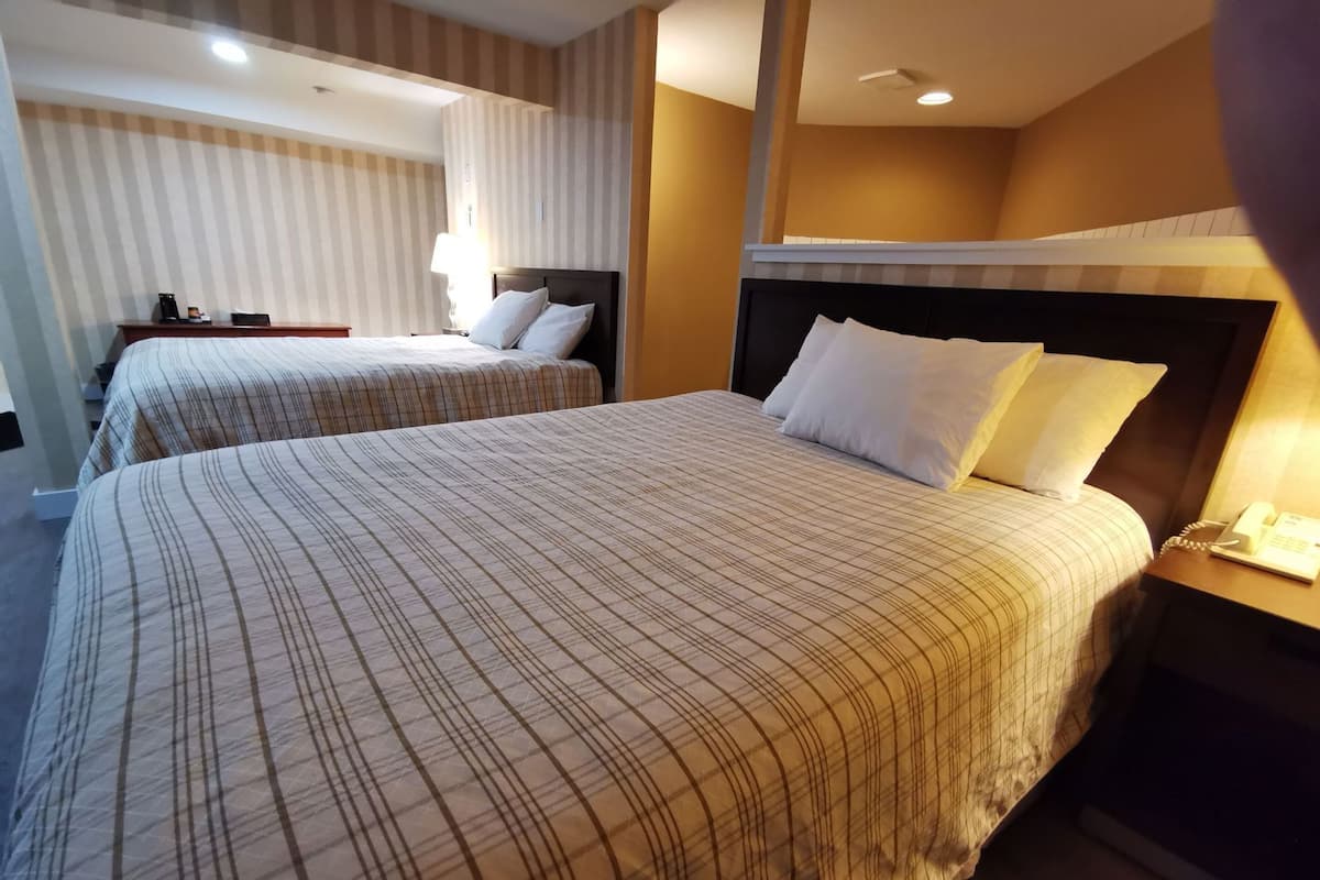 A hotel room with two beds, a nightstand with a phone, and a wall-mounted lamp.