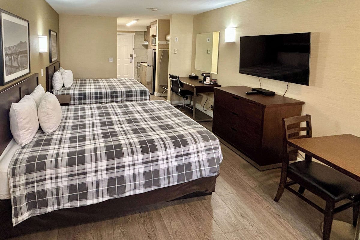 A hotel room with two beds, a desk, a TV, and a dining table.