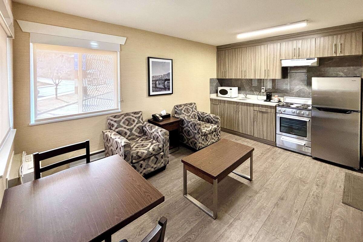 A compact kitchen with modern appliances, a dining area with patterned chairs, and a large window providing natural light.
