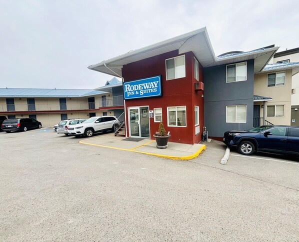 A motel with a red and grey exterior, a parking lot with several cars, and a sign reading "Rodeway Inn & Suites". - Rodeway Inn & Suites (Kamloops)