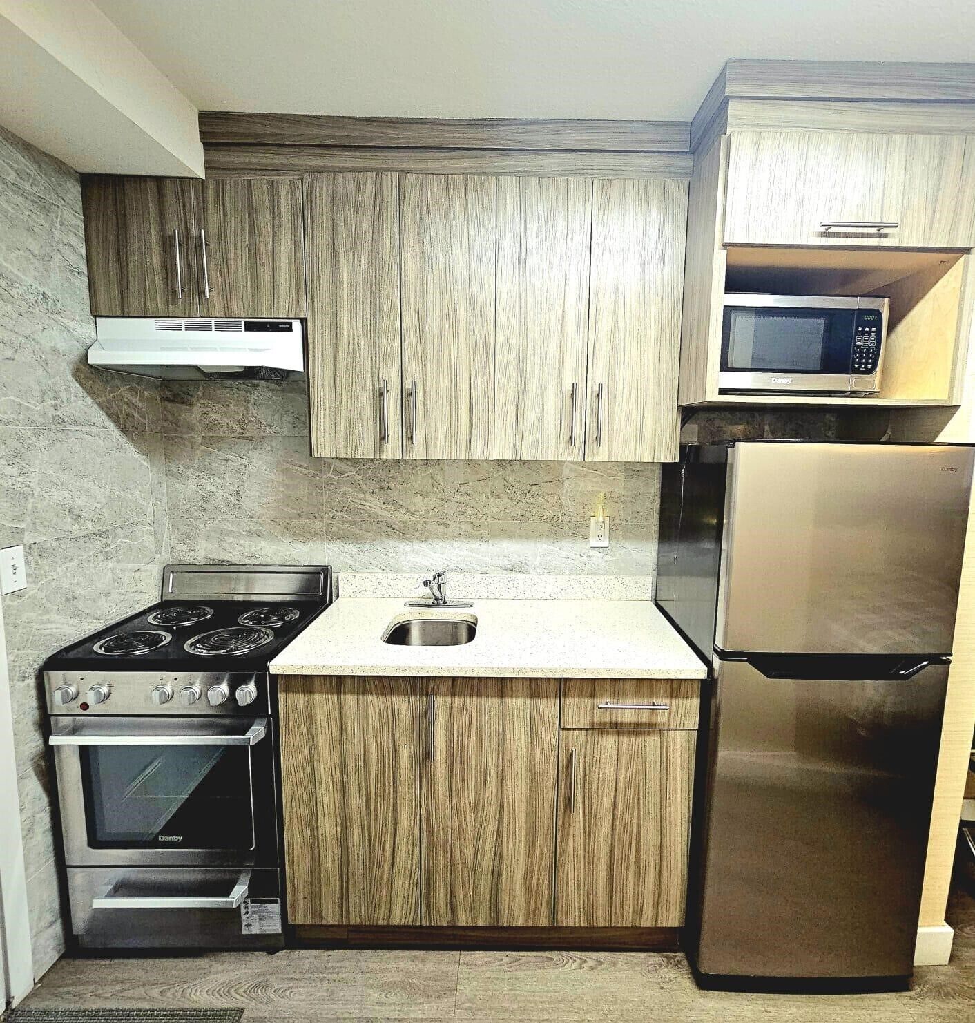 A compact kitchen with wooden cabinets, a stainless steel stove, a microwave, and a refrigerator.