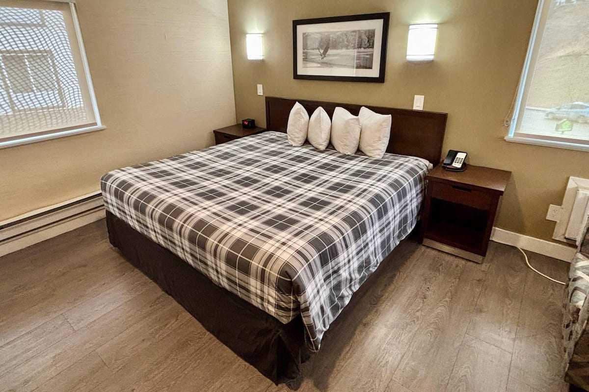 A bedroom with a large bed, a nightstand, a wall-mounted phone, and a framed picture above the bed.