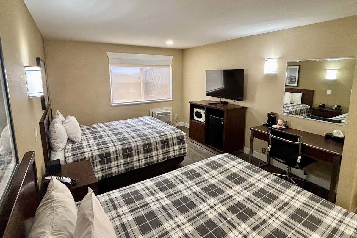A hotel room with two beds, a TV, a desk with a computer, a microwave, and a mirror.