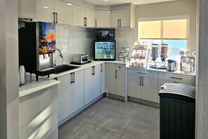 A modern kitchen with white cabinets, a microwave, a toaster, and a coffee machine. - Rodeway Inn & Suites (Kamloops)