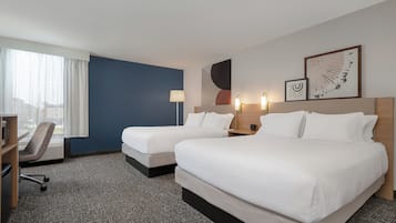 A hotel room with two beds, a desk, a chair, and a large window with curtains.